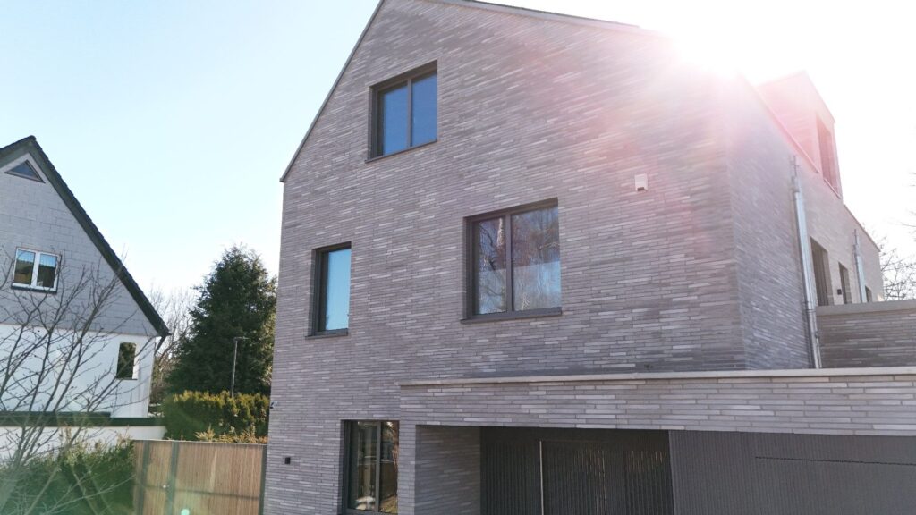 Moderní dům s klinkerovou páskovou fasádou a velkými okny v rezidenční čtvrti za slunečného dne