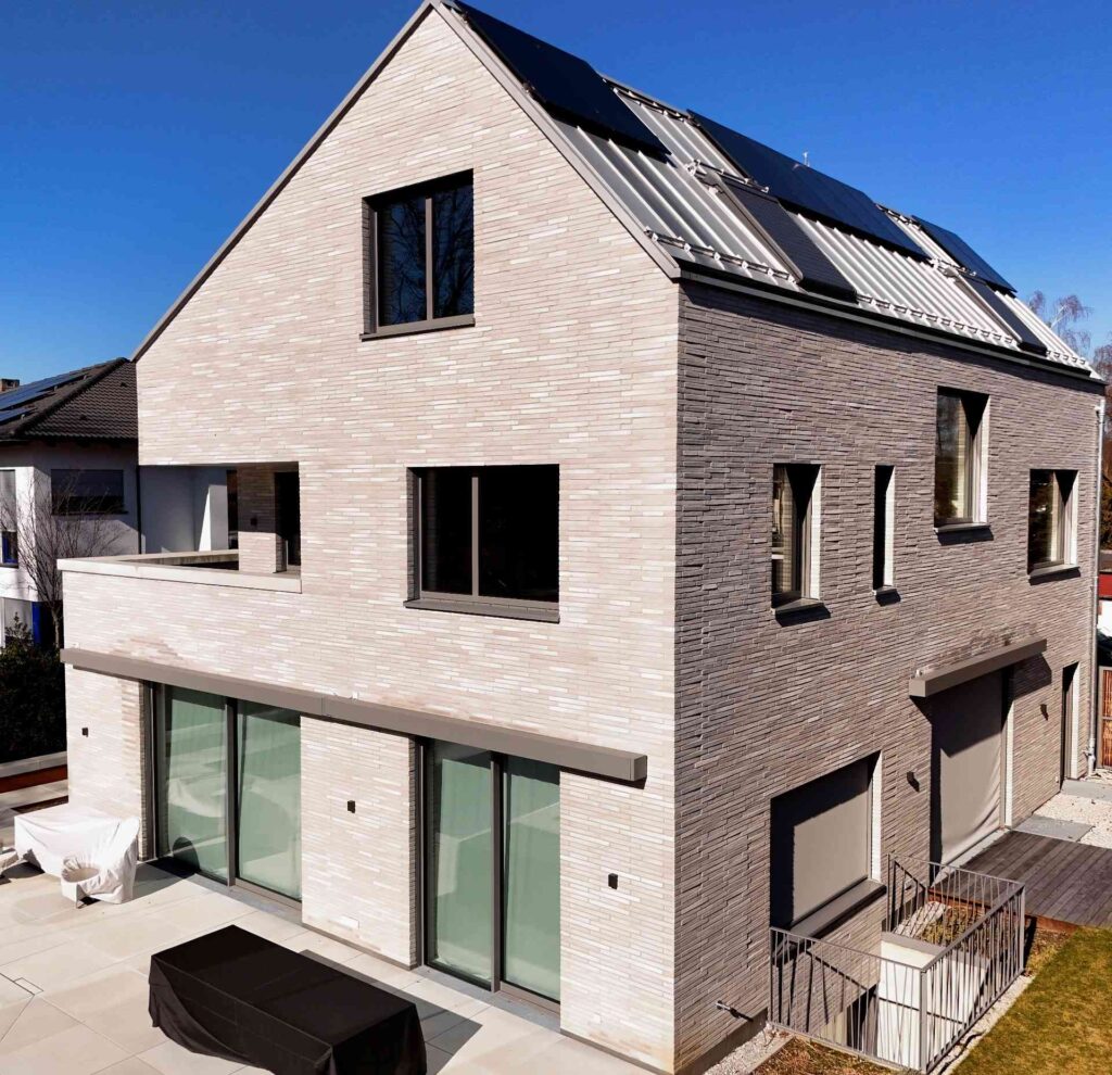 Moderní rodinný dům s klinkerovou páskovou fasádou a solárními panely na střeše pod modrým nebem