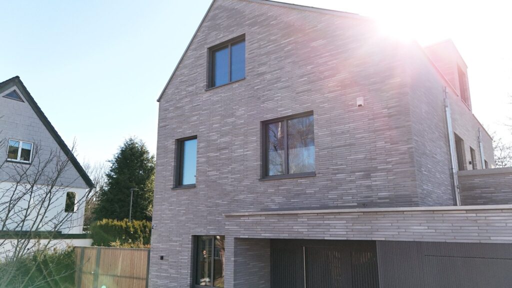 Moderní dům s fasádou z klinkerových pásků a dřevěnými okenními rámy v rezidenční zástavbě