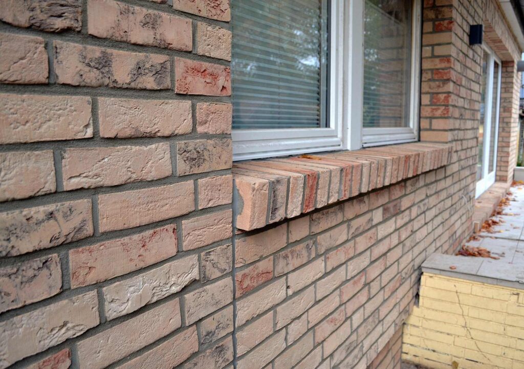 Fasáda domu z klinkerových pásků s okny a parapety, detail cihlové obkladové fasády