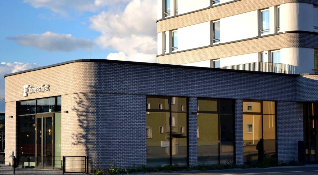 Moderní budova s klinkerovou páskovou fasádou v tmavých a světlých tónech, velká okna a fitness centrum