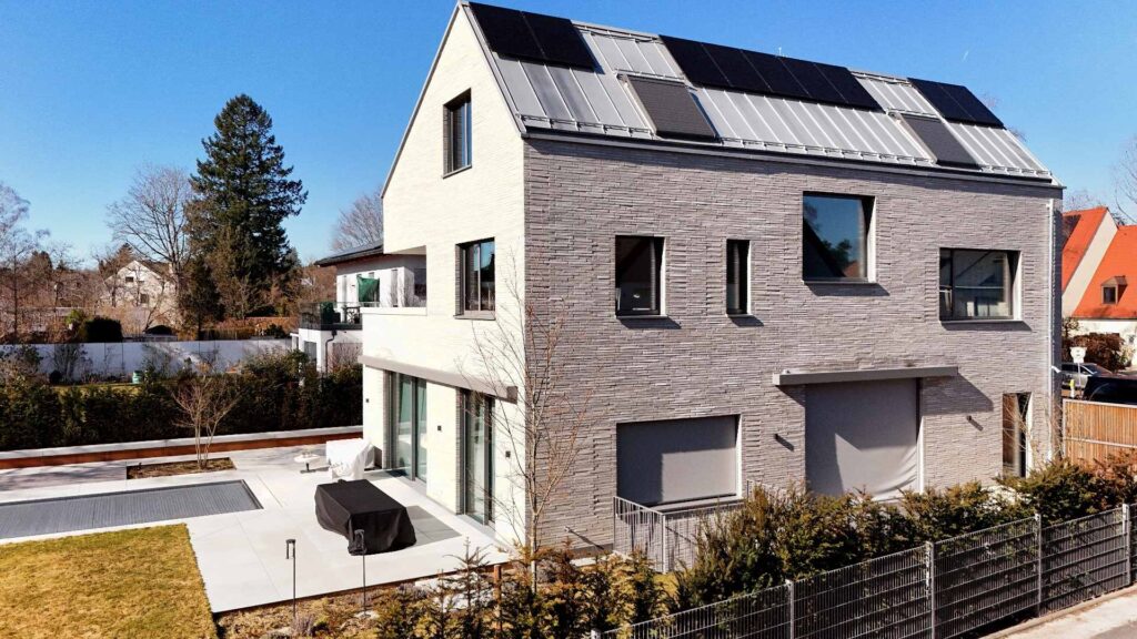 Moderní dům s klinkerovou páskovou fasádou a solárními panely na střeše, zahrada s terasou