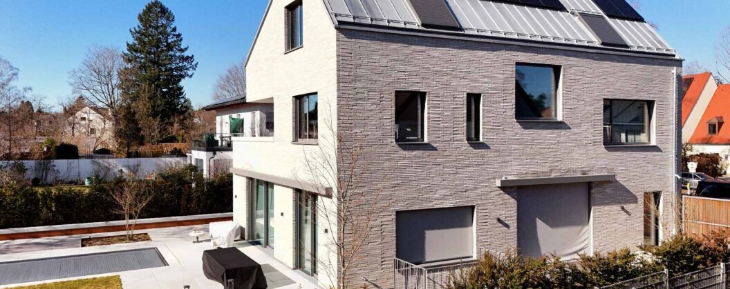 Moderní dům s klinkerovou páskovou fasádou a solárními panely na střeše, zahrada s terasou