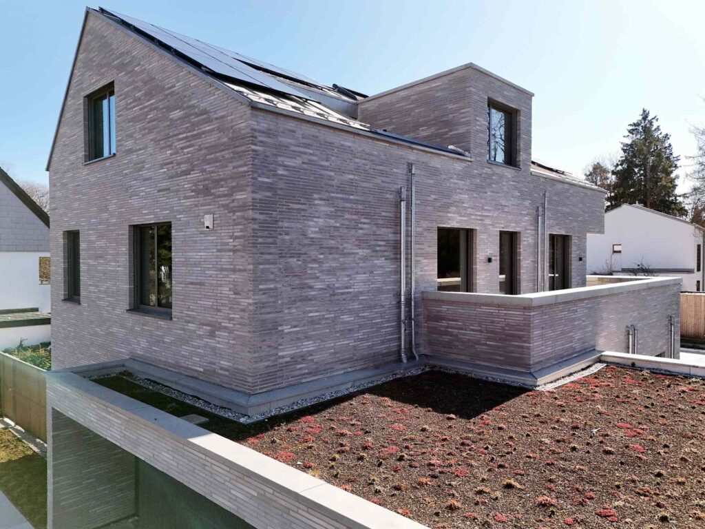 Moderní dům s fasádou z klinkerových pásků v šedém odstínu, zelená střecha a velká okna