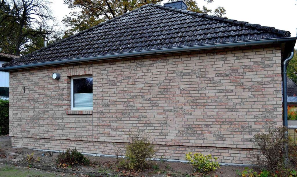 Moderní rodinný dům s klinkerovou páskovou fasádou a tmavou střešní krytinou obklopený zelení