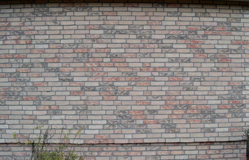 Fasáda z klinkerových pásků v odstínech béžové, červené a šedé s rostlinami u základu budovy