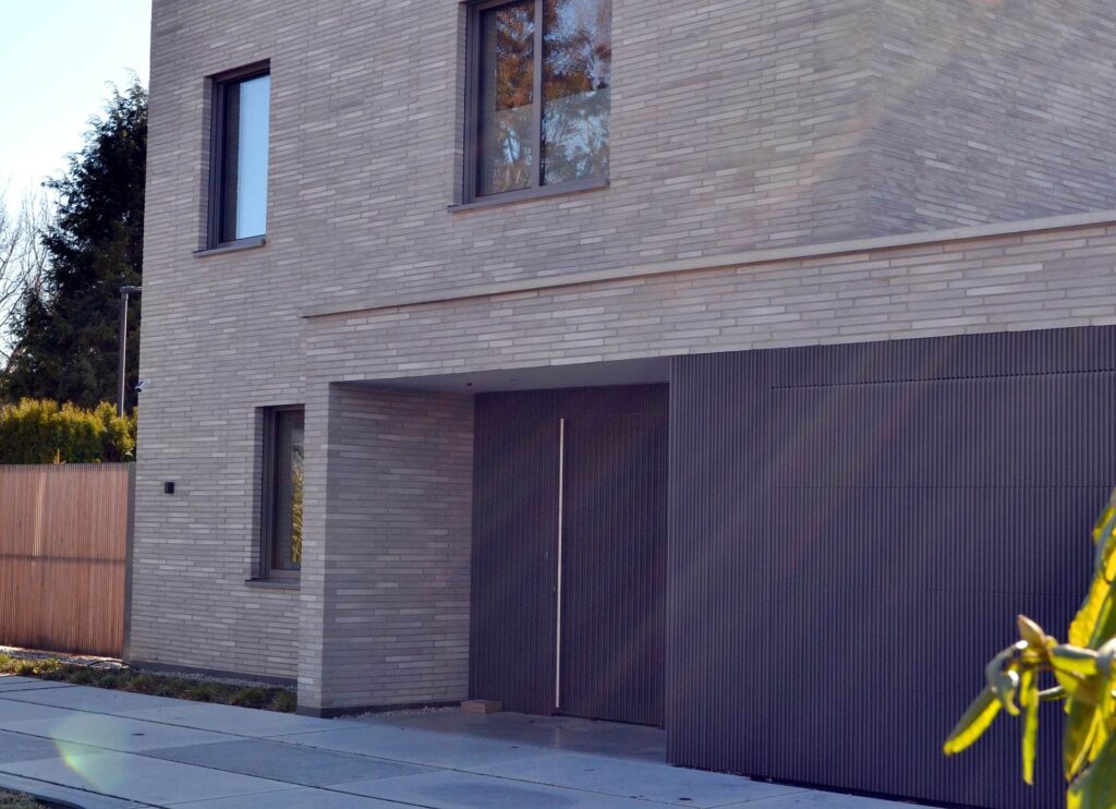 Moderní dům s klinkerovou páskovou fasádou a tmavou garáží, kombinace cihlových pásků a dřevěných prvků