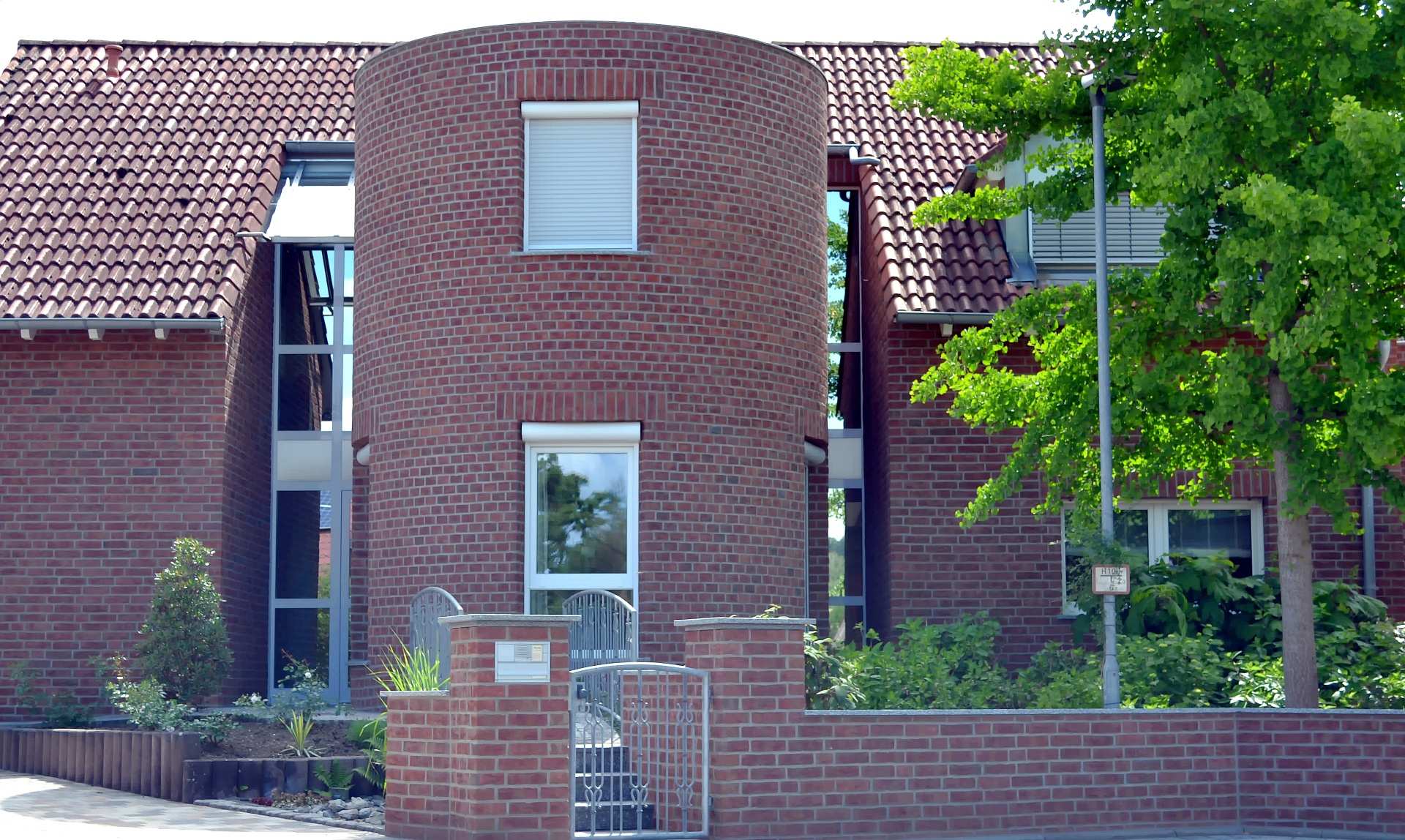 Moderní dům s klinkerovou páskovou fasádou, cihlovou zdí a červenou střešní krytinou obklopený zelení