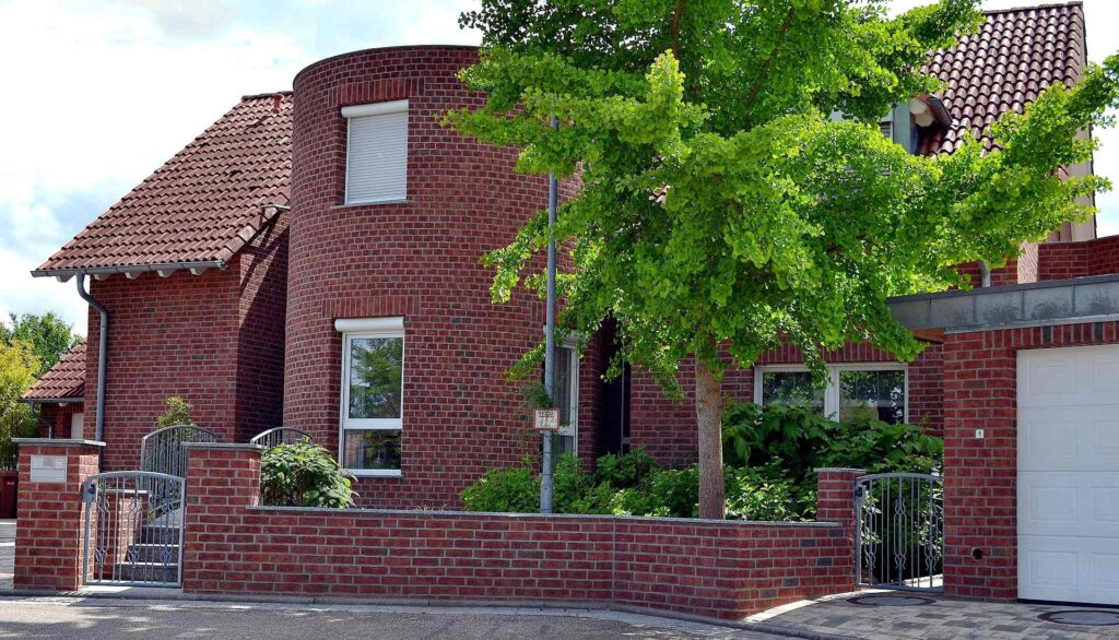 Moderní rodinný dům s klinkerovou páskovou fasádou, cihlovou zdí a červenou taškou střechou, obklopený zelení.