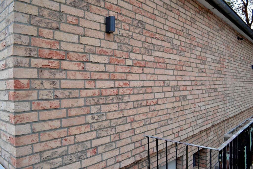 Fasáda z klinkerových pásků v odstínech béžové a červené s černým světlem na cihlové zdi domu