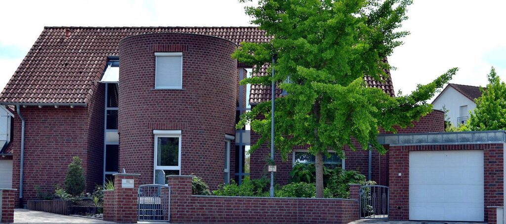 Moderní dům s klinkerovou páskovou fasádou a cihlovou zdí, obklopen zelení a s garážovými vraty