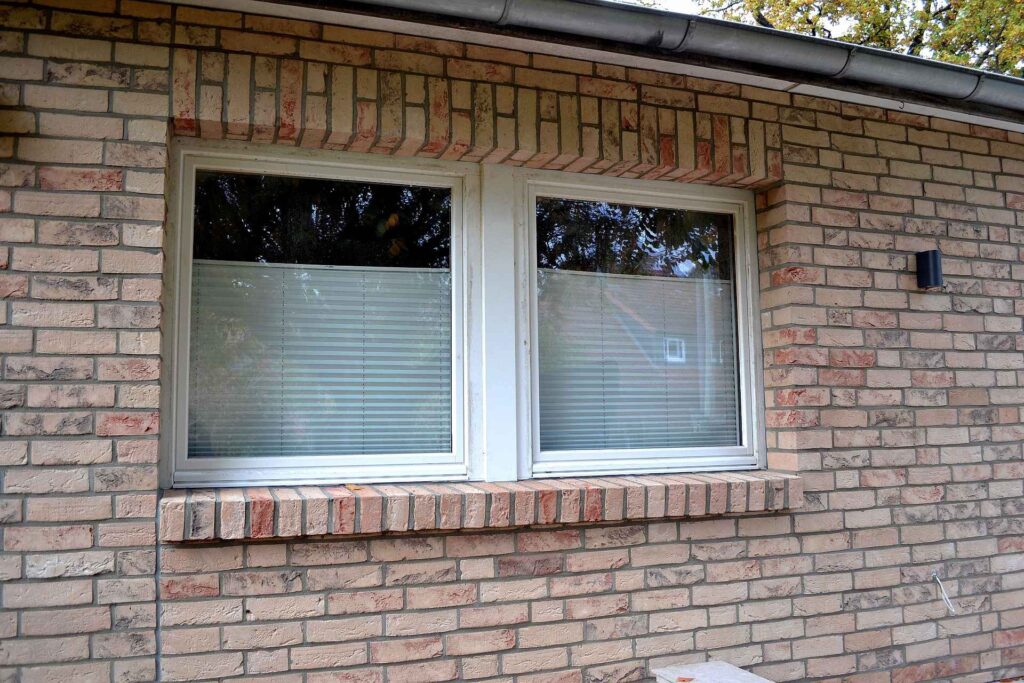 Fasáda domu s klinkerovými pásky a dvěma okny s žaluziemi, cihlová pásková fasáda v přírodních tónech