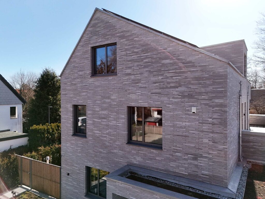 Moderní dům s klinkerovou páskovou fasádou v šedohnědých tónech, velkými okny a současnou architekturou