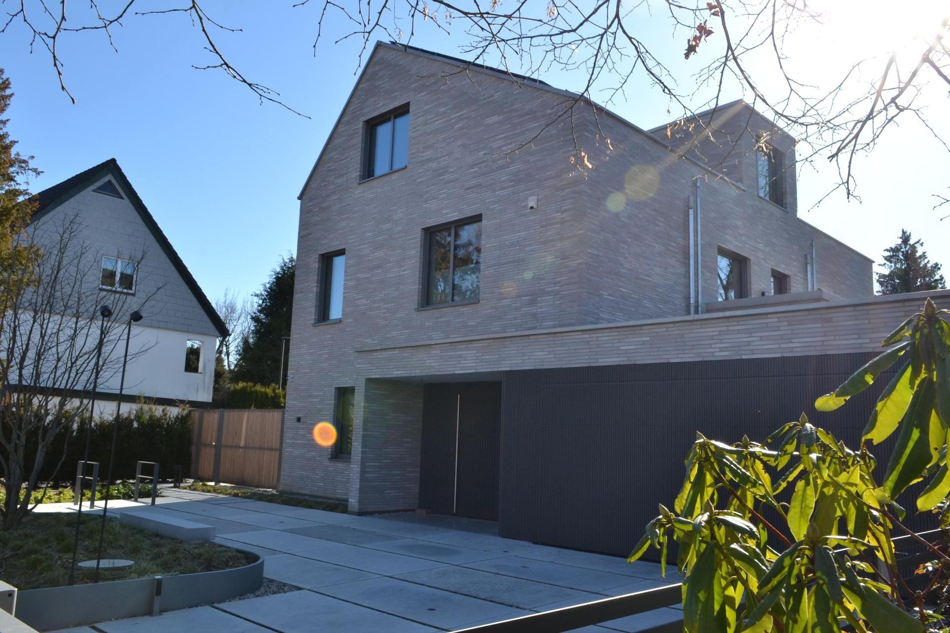 Moderní dům s fasádou z klinkerových pásků, dvougaráž a upravenou zahradou pod jasnou oblohou