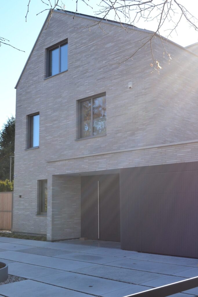 Moderní dům s fasádou z klinkerových pásků v béžové barvě, velká okna a dřevěný obklad v přízemí