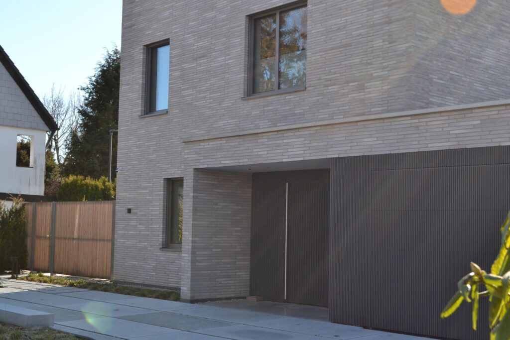 Moderní dvoupodlažní dům s klinkerovou páskovou fasádou a integrovanou garáží s tmavými vraty