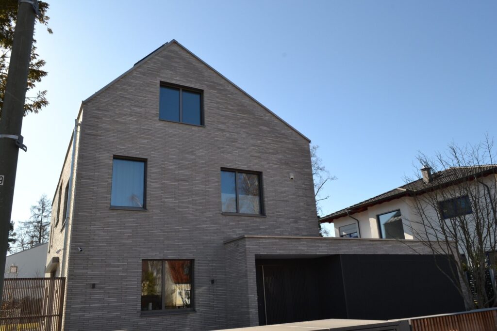 Moderní rodinný dům s klinkerovou páskovou fasádou a tmavými okny pod modrým nebem