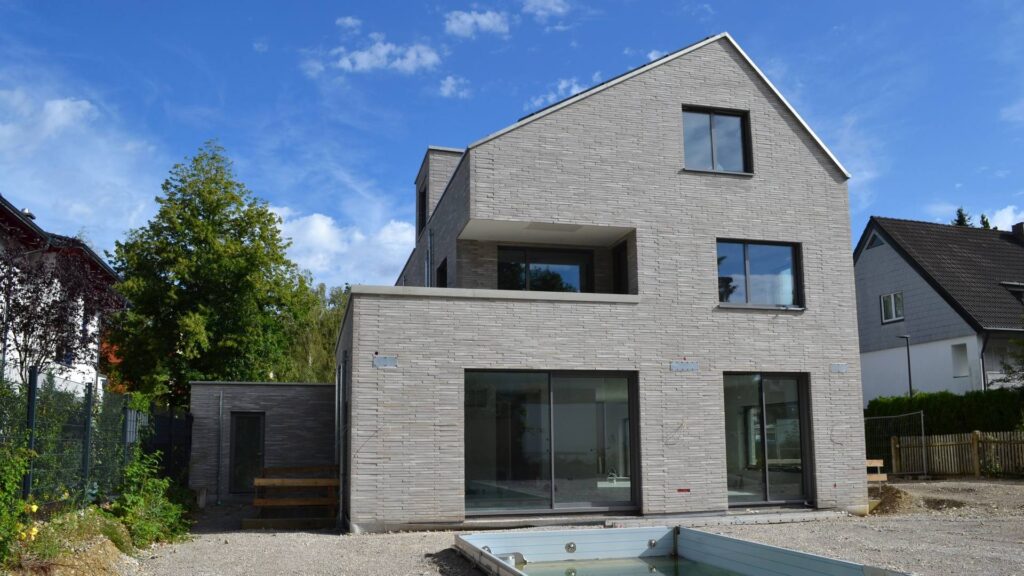 Moderní rodinný dům s klinkerovou páskovou fasádou a velkými okny v rezidenční čtvrti