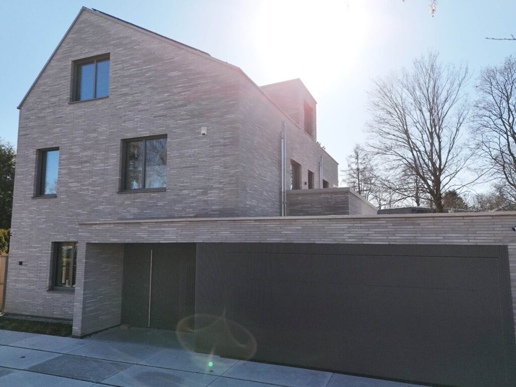 Moderní dům s fasádou z klinkerových pásků a velkými okny, obklopen stromy při západu slunce