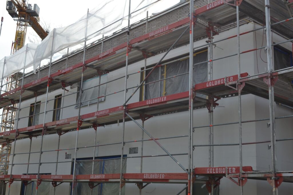 Zateplení fasády domu s lešením a ochrannou plachtou během stavebních prací na bytovém domě