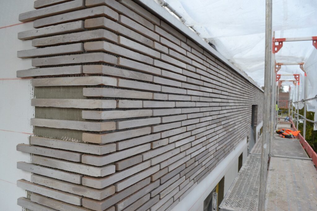 Fasáda z klinkerových pásků během výstavby - detail rohového spojení cihlové páskové fasády na lešení