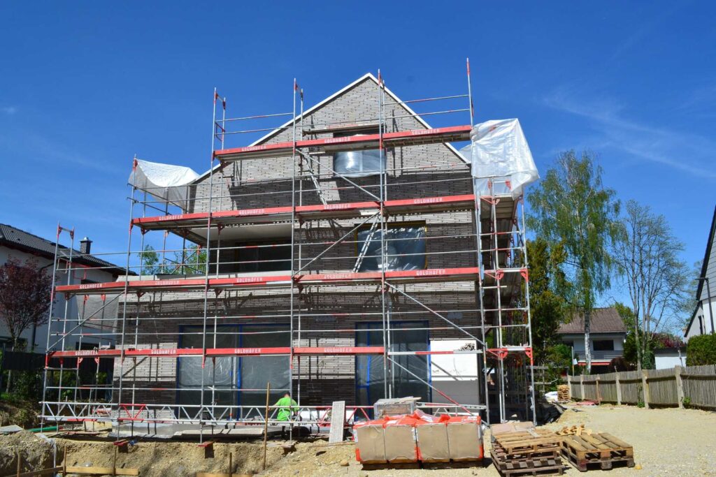 Dům ve výstavbě s lešením a klinkerovou páskovou fasádou, zateplení fasády probíhá na rodinném domě