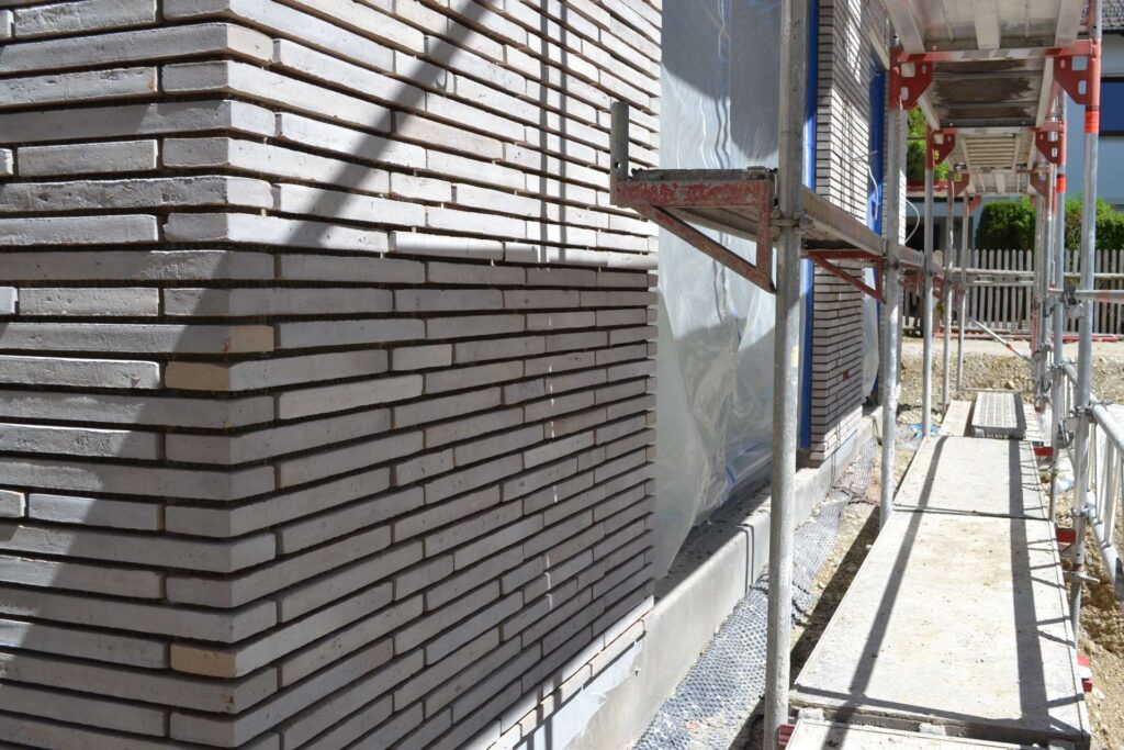 Výstavba domu s fasádou z klinkerových pásků, lešení kolem budovy během zateplování fasády