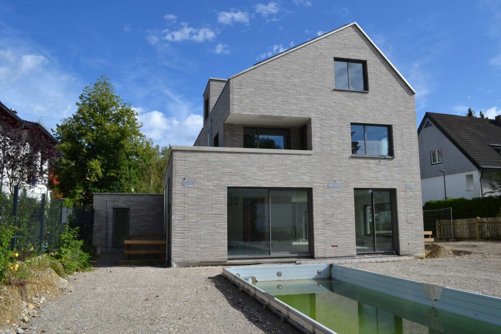 Moderní rodinný dům s klinkerovou páskovou fasádou a velkými okny, zahrada s vodním prvkem