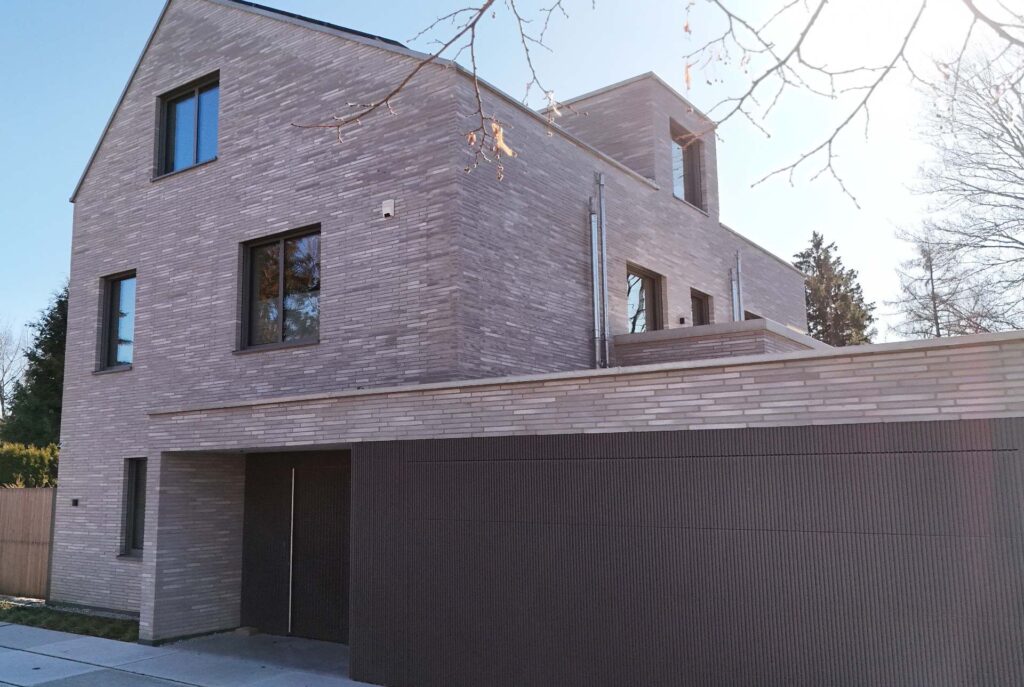 Moderní dům s klinkerovou páskovou fasádou a tmavou garážovou bránou v podzimním prostředí