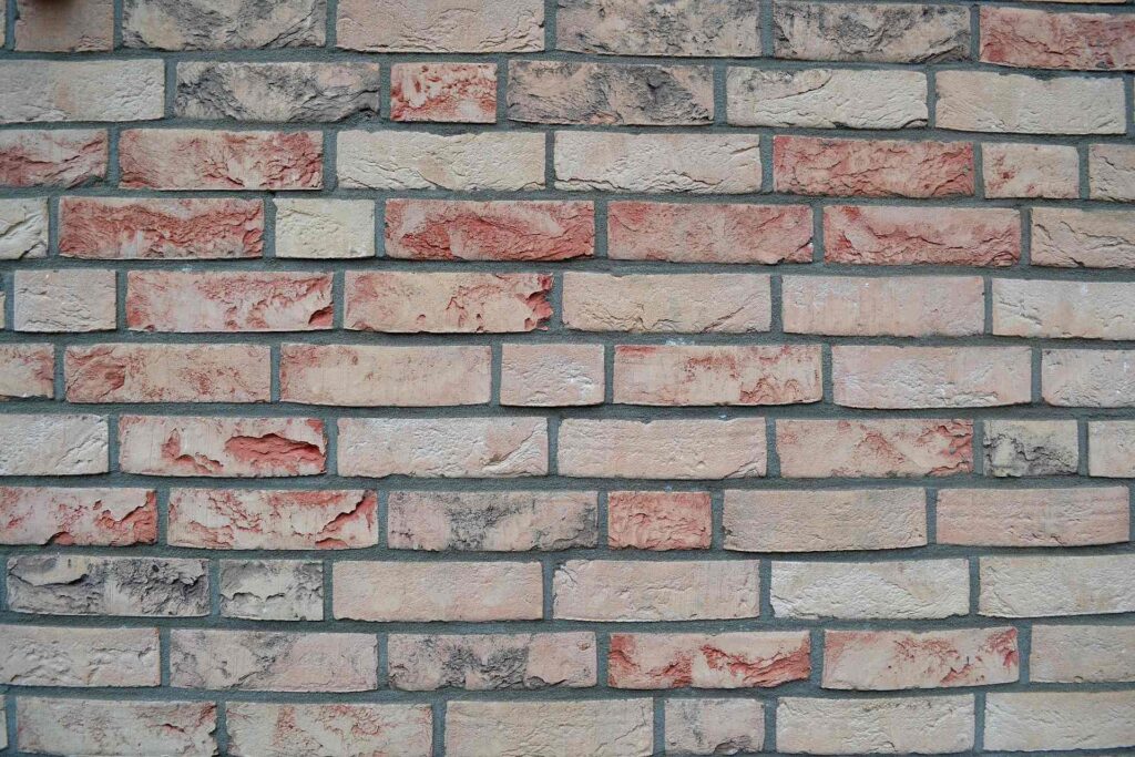 Klinkerová pásková fasáda s béžovo-červenými obkladovými pásky a šedými spárami na zateplené stěně