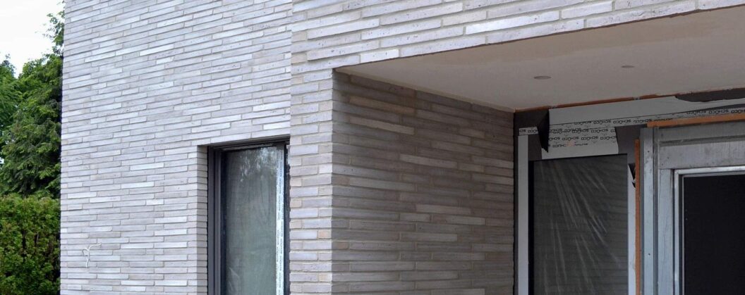 Moderní dům s fasádou z klinkerových pásků v bílé a hnědé barvě, zakryté okno plastovou folií