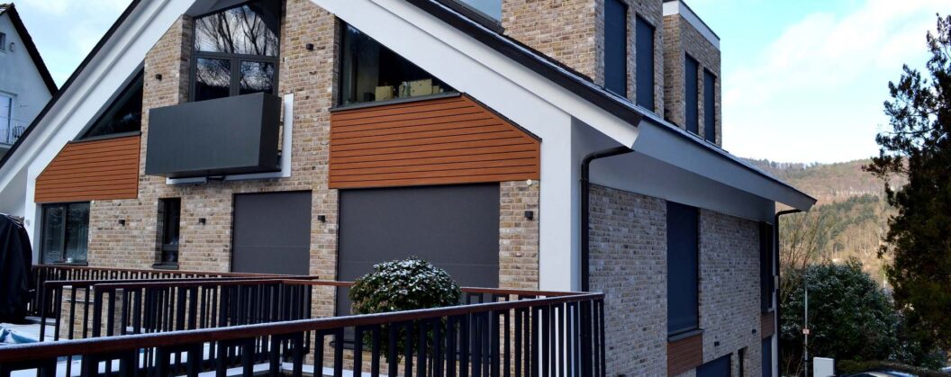 Modernes Einfamilienhaus mit Klinkerfassade und Holzelementen, umgeben von schwarzem Metallzaun